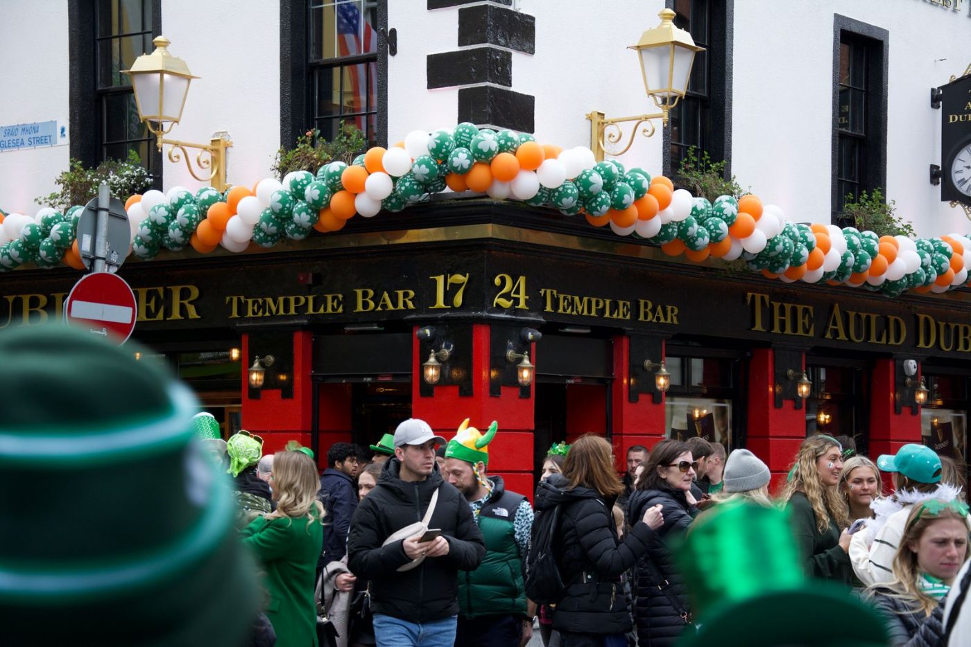 Fachada do pub The Temple Bar, em Dublin, decorada com balões verdes, brancos e laranja, e multidão de chapéus verdes no St. Patrick's Day
