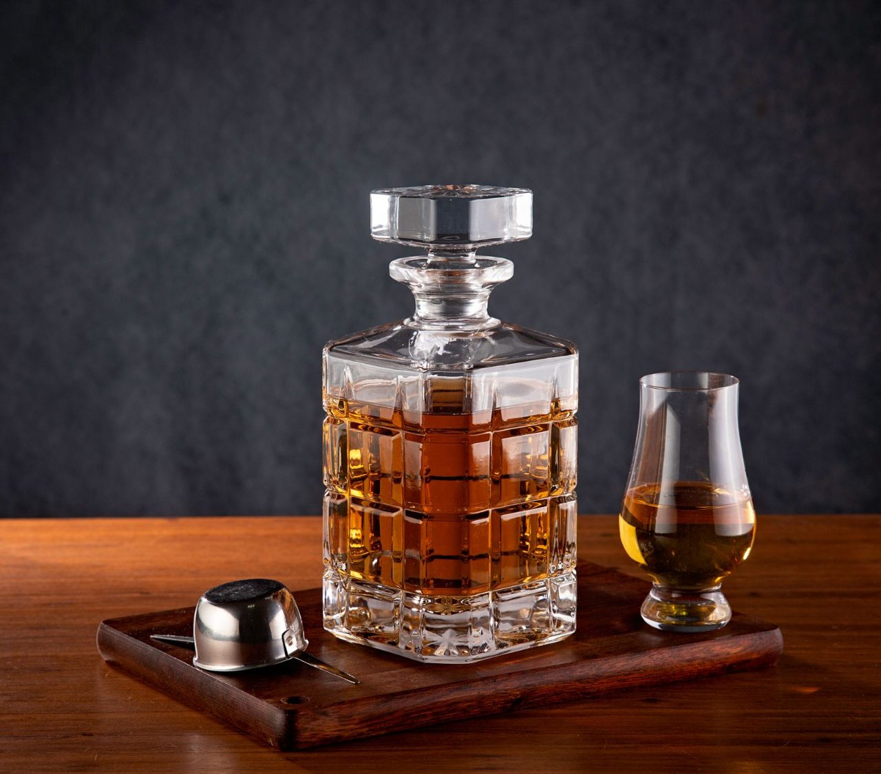 Licoreira de cristal com whiskey e um copo de degustação sobre uma bandeja de madeira